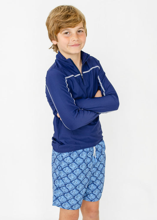 A boy wearing the sun protective Boys Navy Sport Zip Top and Boys Seaside Swim Trunk from Cabana Life with his arms crossed.