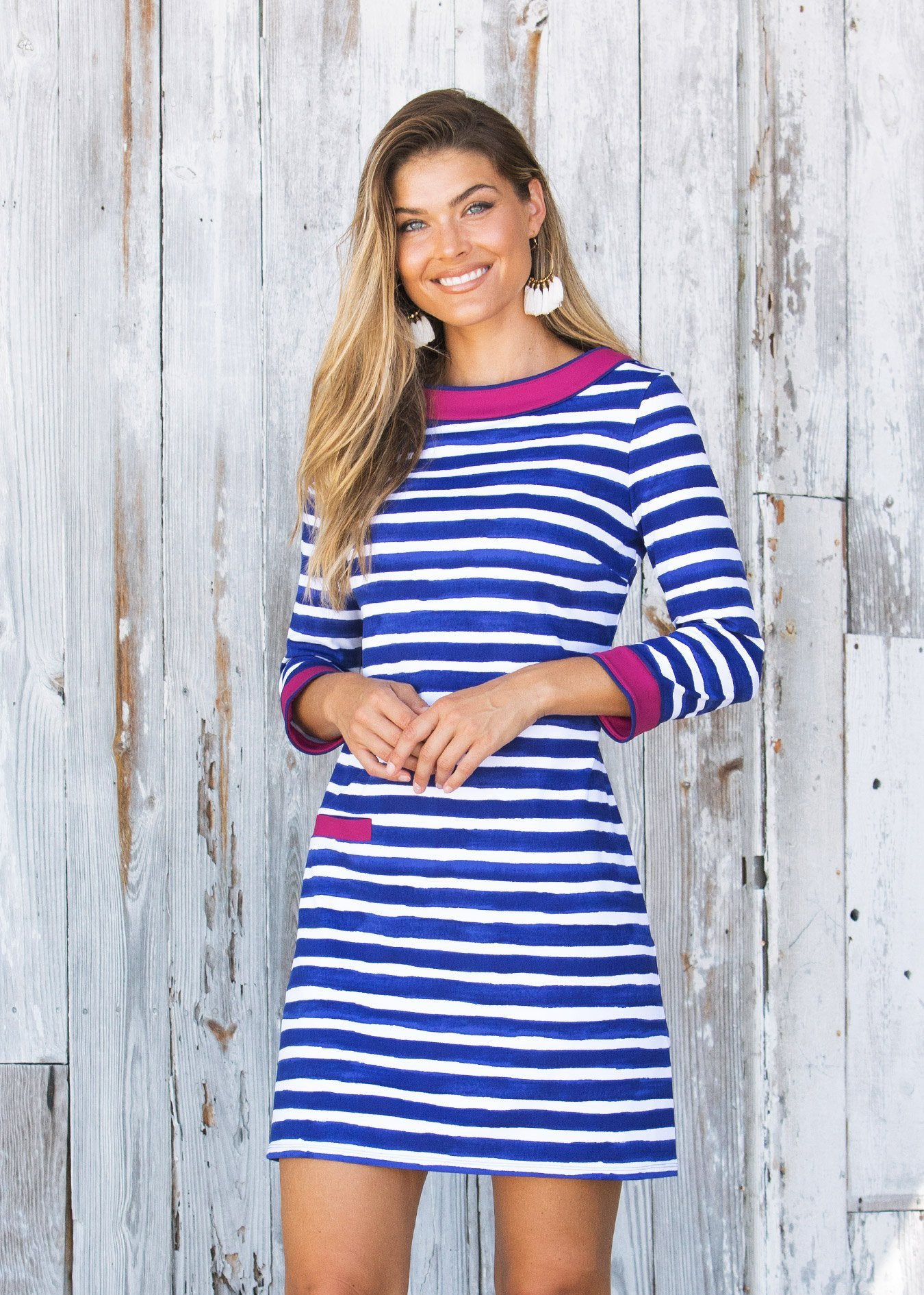 Blonde woman in front of grey wood wall with hands in front wearing Cabana Life's sun protective Watercolor Stripe Cabana Shift Dress.