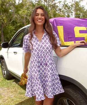 A brunette woman smiling while wearing the sun protective Cabana Life Purple Short Sleeve Tiered Dress in front of a white truck.