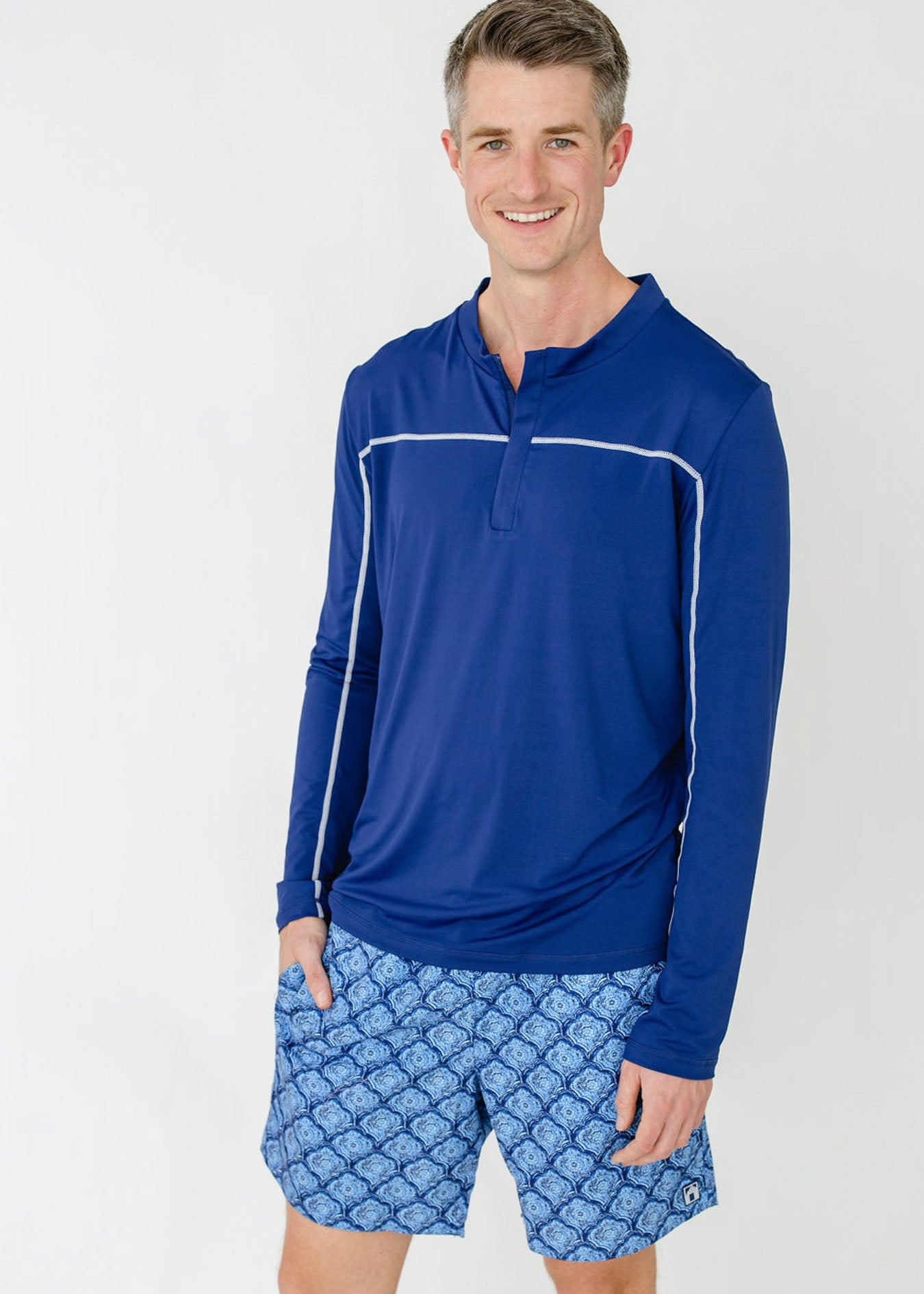 A man smiling while wearing the sun protective Men's Navy Sport Zip Top and Men's Seaside Swim Trunk from Cabana Life.