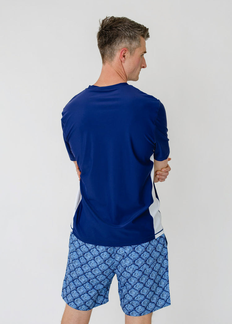 The back of a man wearing the sun protective Men's Navy Short Sleeve Rashguard with the Men's Seaside Swim Trunk from Cabana Life.