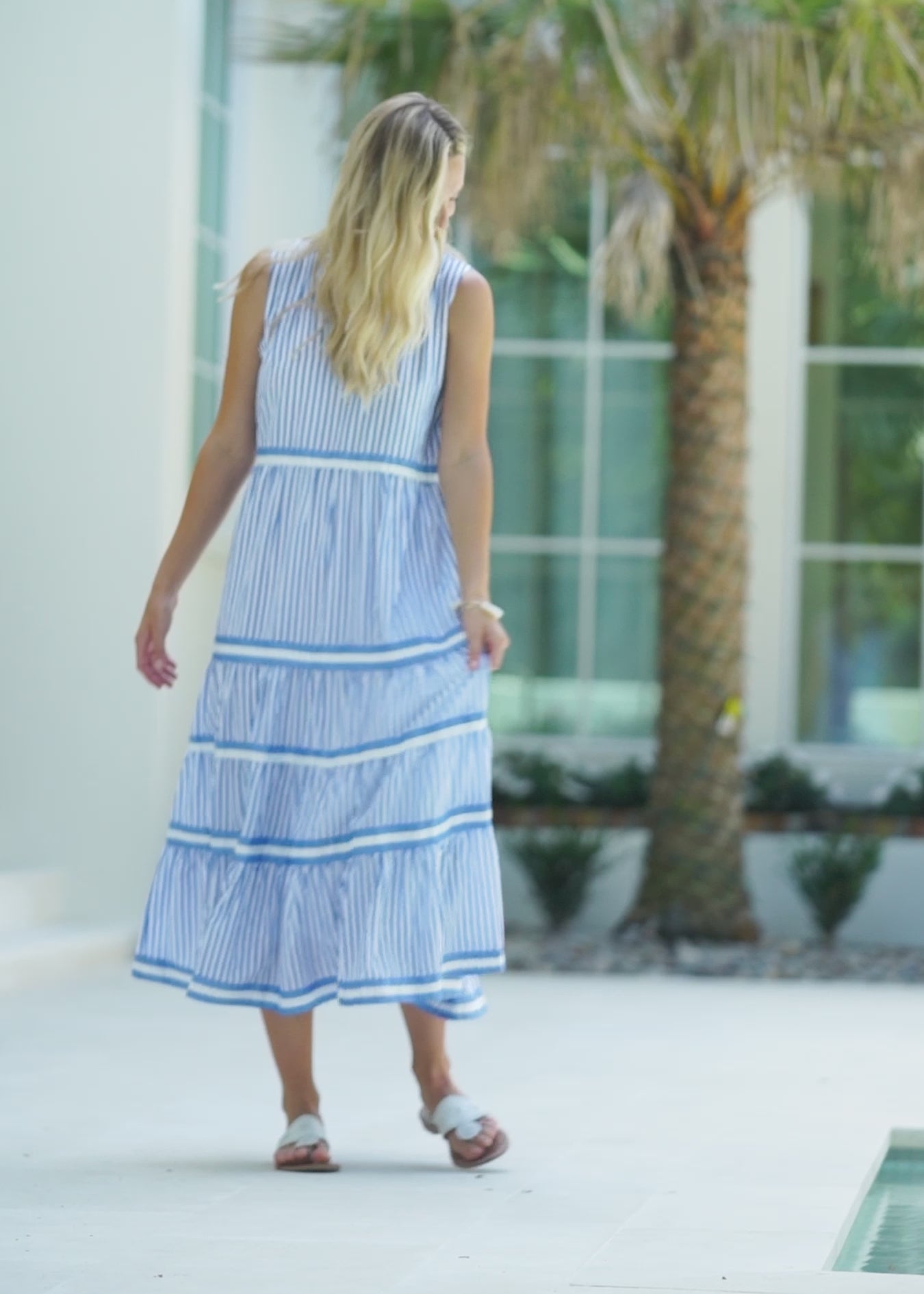 A blonde woman outside wearing the flowy sun protective Palm Beach Sleeveless Tiered Maxi Dress from Cabana Life.